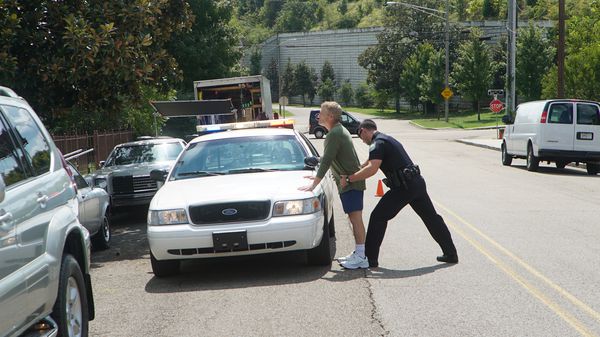 Reconstruction actor police officer arresting man by car.